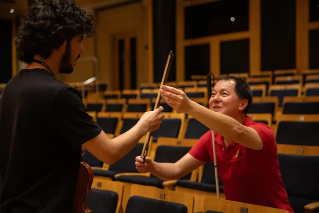 Uma pessoa com deficiência visual toca uma batuta de maestro apresentada por um educador da Fundação Osesp.