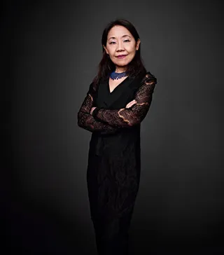 Cely Kozuki is an Asian woman with long black hair. She is wearing a black dress and a blue necklace.