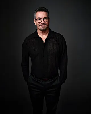 Jocelyn is a white man with a goatee and gray hair. He is wearing a black shirt and a silver necklace with a small green pendant. He is also wearing glasses.