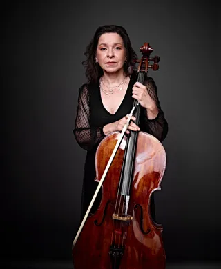 Maria Luisa is a white woman with brown hair and light-colored eyes. She is wearing a low-cut black dress with sheer sleeves, a silver necklace, and holding a cello.