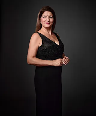 Roxana is a white woman with long blonde hair. She is wearing dark pink lipstick and small sparkling earrings.