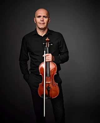 Simeon Grinberg is a bald white man. He is wearing a black shirt and holding a viola.