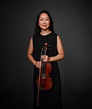 Sung Eun Cho é uma mulher coreana de cabelos longos. Ela está usando um vestido preto sem alças e segurando um violino.