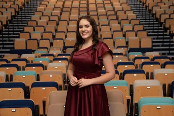 Pollyana Santana é uma mulher branca, de cabelos longos e castanhos. Ela usa um vestido vinho e sorri.