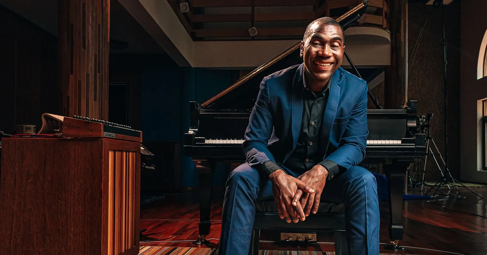 Hercules Gomes é um homem negro e calvo. Ele está sentado em um banco de piano e sorri.