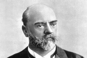 Retrato em preto e branco do compositor tcheco Antonín Dvořák. Ele aparece com expressão séria, barba cheia e bigode espesso, vestindo paletó escuro e colarinho alto. A imagem tem o estilo clássico das fotografias do século XIX.