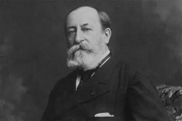 Retrato em preto e branco de Camille Saint-Saëns, com expressão serena, barba longa e cabelos ralos. Veste paletó escuro com lenço no bolso, posando sentado diante de fundo neutro e sóbrio.